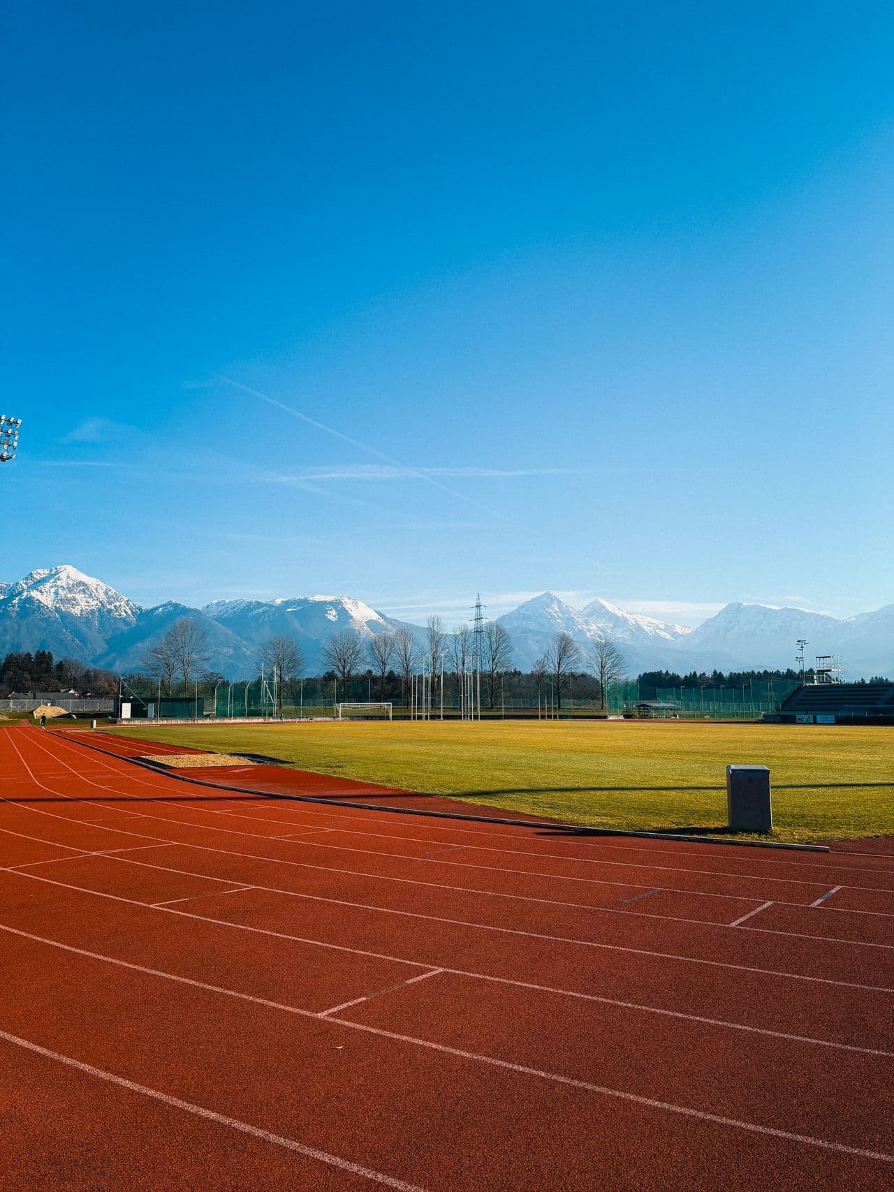 Piste d'athlétisme en tartan avec un stade en herbe et des montagnes enneigées en arrière-plan
